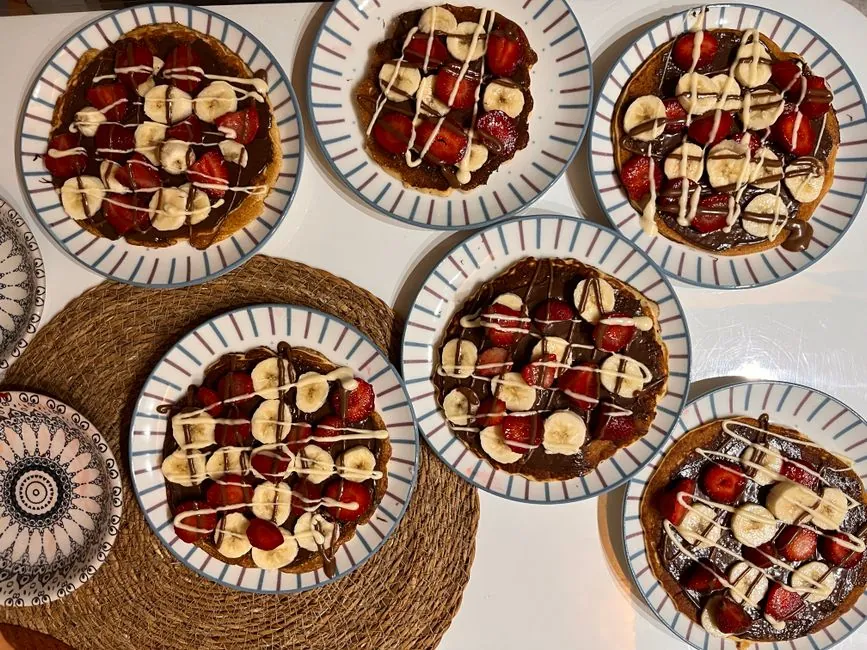 Top view of chocolate-drizzled pancakes with bananas and strawberries on plates.