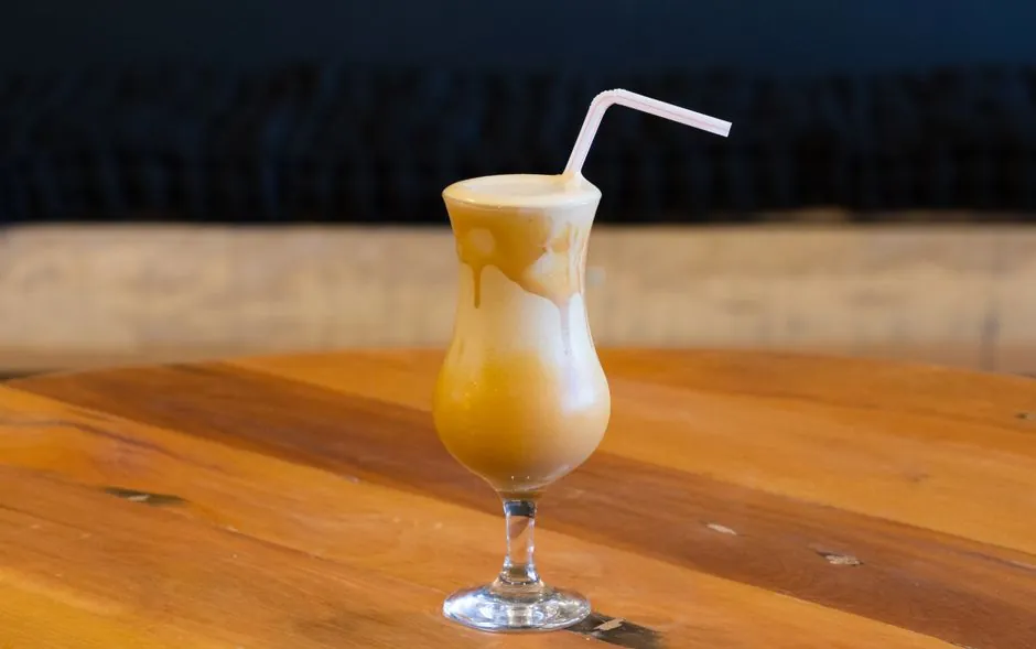 A mouthwatering caramel milkshake with a straw in a glass, set on a wooden table.