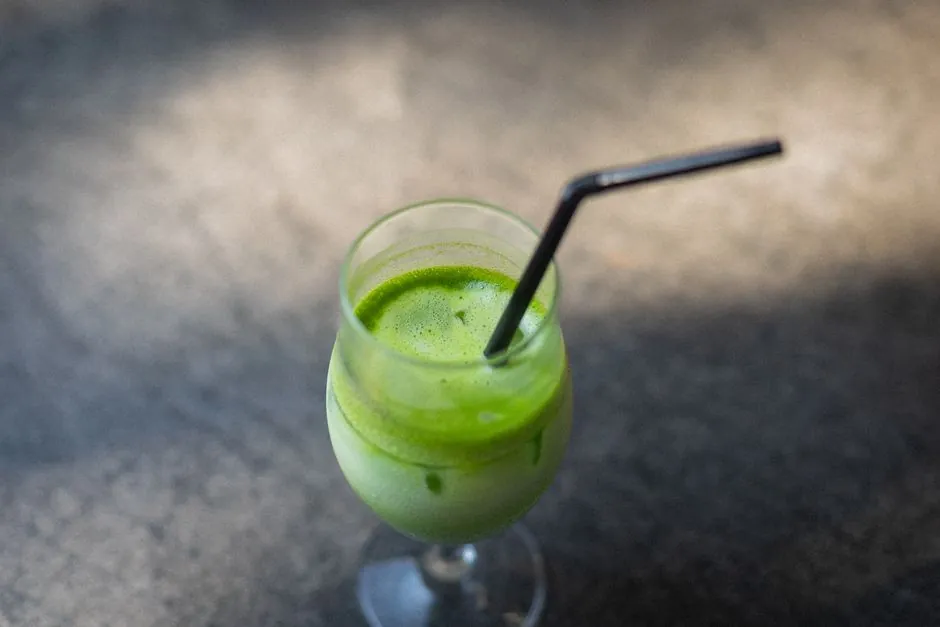 Top-down view of a refreshing iced matcha latte in a glass with a black straw on a textured surface.