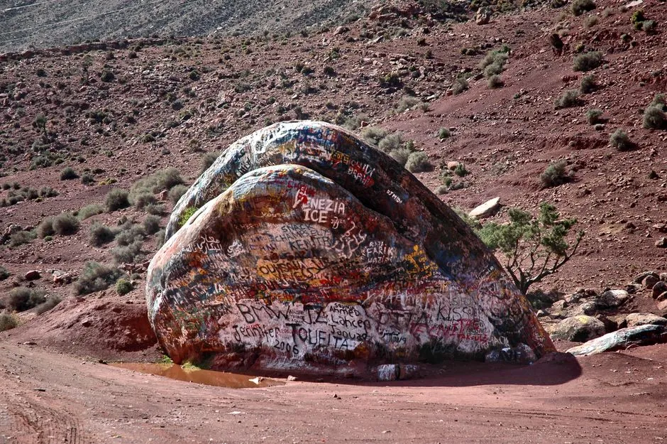 Large rock adorned with colorful graffiti in the Agadir desert landscape, Morocco.