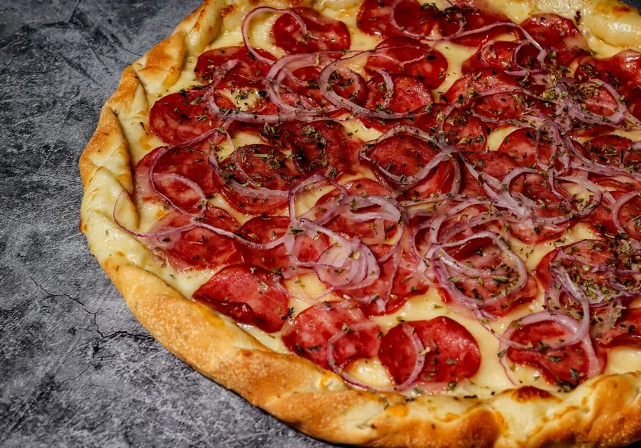 Close-up of a pepperoni pizza with onions on a textured surface in Rio de Janeiro, Brazil.
