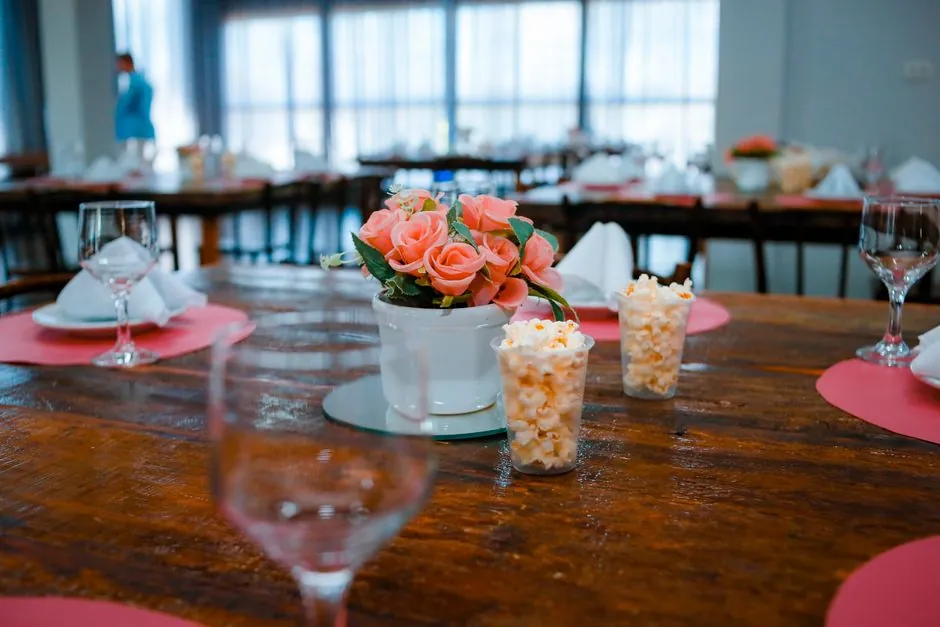 An elegant indoor table setting featuring a pink rose centerpiece, popcorn, and wine glasses.