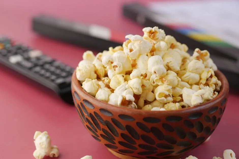 A delicious bowl of popcorn with remote and document on a pink surface, perfect for movie nights.