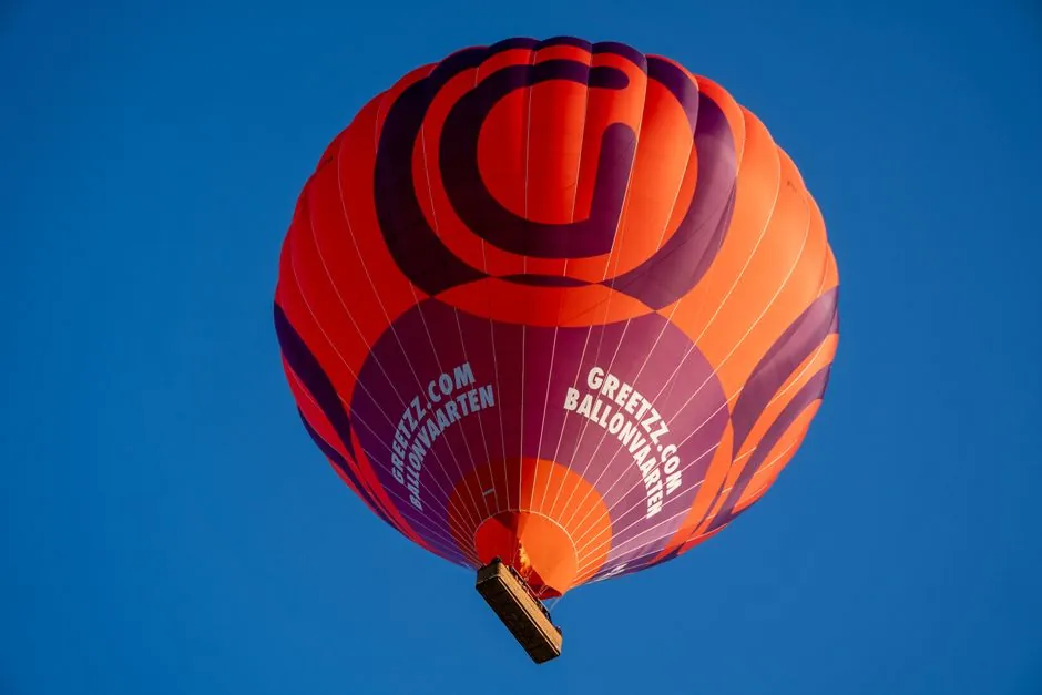 Bright orange hot air balloon with purple graphics floating against a clear blue sky.