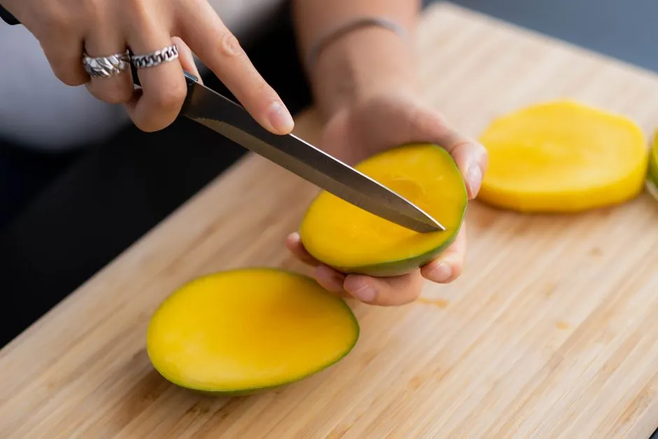 Close-up of hands slicing mangoes on a cutting board, highlighting fresh tropical fruit preparation.